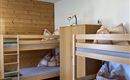 A cozy room with bunk beds and wooden paneling. A bright lamp hangs from the ceiling and there are several pillows on the beds.