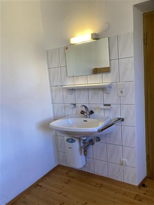 A modern bathroom with a sink and a large mirror. The walls are tiled and the floor is made of wood.