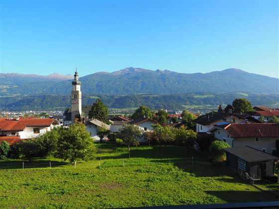 A picturesque landscape with a small village and a church in the foreground. In the background, the mountains stretch under a clear blue sky.