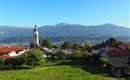 A picturesque landscape with a small village and a church in the foreground. In the background, the mountains stretch under a clear blue sky.