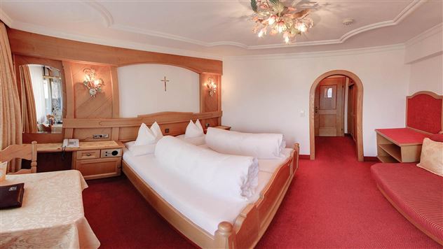 Une chambre d'hôtel douillette avec deux lits, un tapis rouge et un décor en bois. La chambre a une atmosphère chaleureuse avec une petite table et un coin salon.