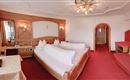 Une chambre d'hôtel douillette avec deux lits, un tapis rouge et un décor en bois. La chambre a une atmosphère chaleureuse avec une petite table et un coin salon.