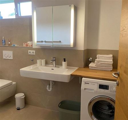 Een moderne badkamer met een wastafel, handdoeken en een wasmachine. Heldere muren en een grote spiegel zorgen voor een vriendelijke sfeer.