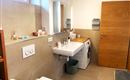 Een moderne badkamer met een wasmachine, een wastafel en houten planken. De muren zijn licht en de vloer is in neutrale tinten gehouden.