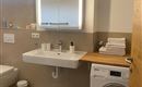 Een moderne badkamer met een wastafel, handdoeken en een wasmachine. Heldere muren en een grote spiegel zorgen voor een vriendelijke sfeer.