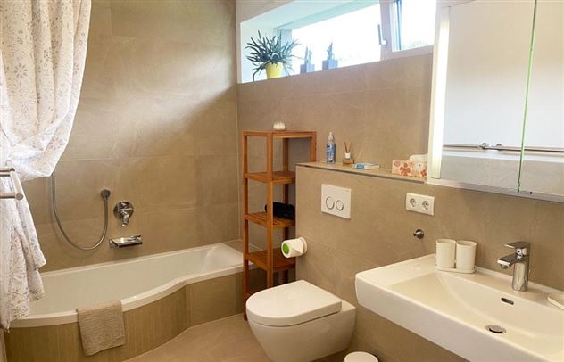 Een moderne badkamer met een badkuip, een wastafel en een toiletgedeelte. Er zijn lichte kleuren en planten die een vriendelijke sfeer creëren.