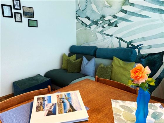 Een gezellige woonkamer met een blauwe bank en kleurrijke kussens. Op de tafel ligt een fotoboek en een vaas met een roos.