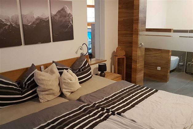 A modern bedroom with a double bed and striped pillows. There are pictures of mountains hanging on the wall, and the room has a warm wooden paneling.