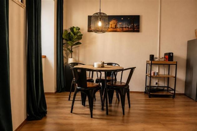 Une salle à manger moderne avec une table ronde et des chaises noires. Au mur, il y a une image et il y a une plante ainsi qu'une lampe élégante.