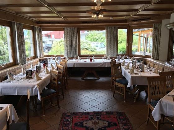 A cozy restaurant with wooden ceilings and large windows. The tables are elegantly set with white tablecloths and cutlery.