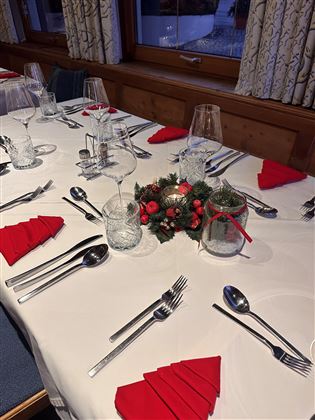 An elegantly set table with red fabric and crystal glasses. In the center of the table is a Christmas wreath with decoration.
