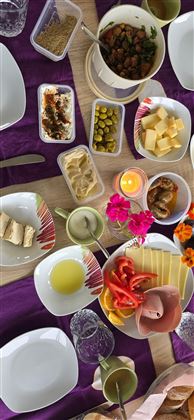 Ein bunter Tisch mit verschiedenen Speisen und Getränken. Es gibt Obst, Käse, Oliven und hübsche Blumen als Dekoration.