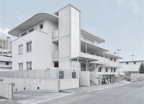 Ein modernes Gebäude mit klaren Linien und einem minimalistischen Design. Die Fassade ist hell und die Umgebung wirkt ruhig und urban.