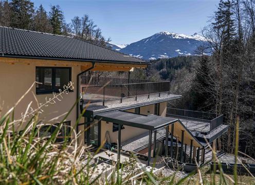 A modern house with terraces amidst a beautiful mountain landscape. In the background, snow-capped mountains and green trees can be seen.