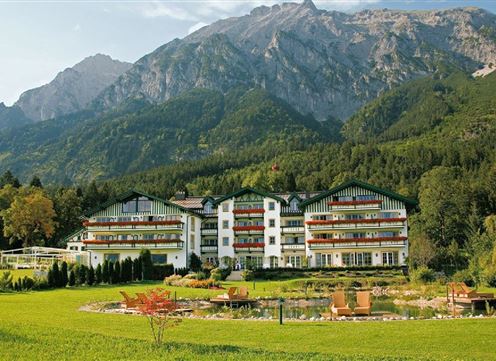 A beautiful hotel in the greenery with a view of majestic mountains. The surroundings feature a tranquil pond and well-maintained gardens.