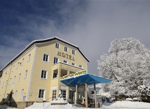 Ein gelbes Hotelgebäude im Schnee mit einer blauen Überdachung am Eingang. Umgeben von schneebedeckten Bäumen und klarem Himmel.