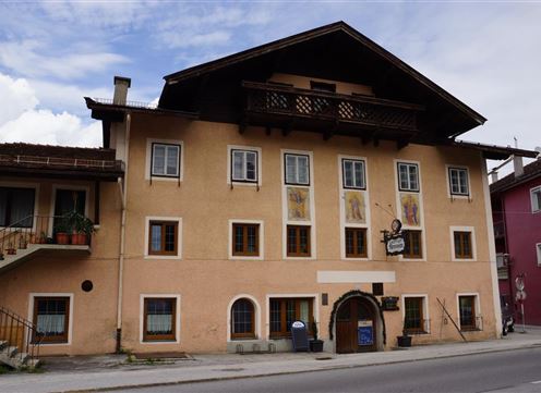 A traditional building with several windows and a balcony. The facade is painted in a light yellow and has some paintings.