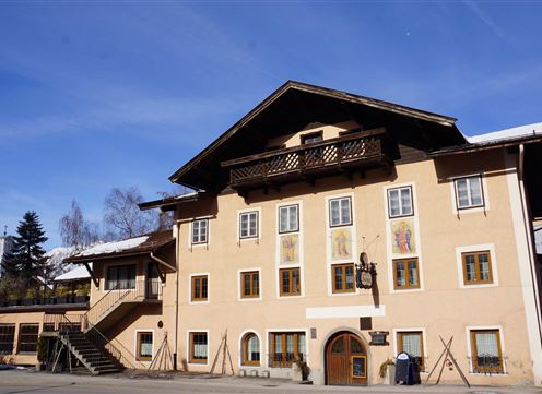 A charming building in alpine style with wooden decorations. The facade is yellow with colorful windows and a clear blue sky in the background.