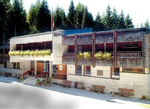 A modern building amidst fir trees. The facade is partially made of wood, with balconies and flower boxes.