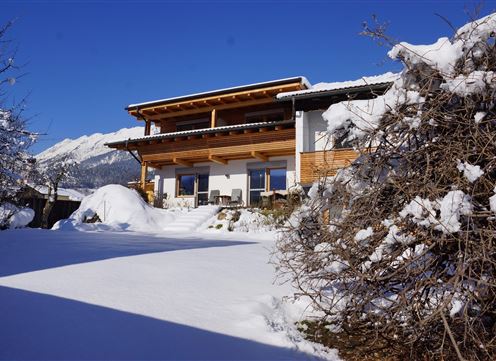 A modern house in the snow with a clear blue sky. The surroundings are snowy and appear wintery peaceful.