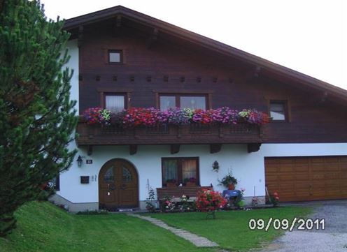 A charming house in alpine style with a wooden upper floor and colorful flowers on the balcony. The pleasant garden and the garage complete the picture.