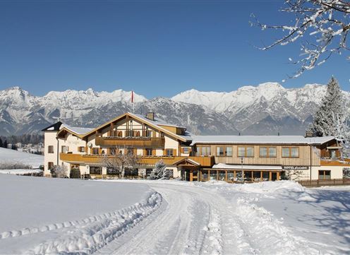 A picturesque hotel in the snow, surrounded by impressive mountain peaks. The clear blue sky creates an inviting winter atmosphere.