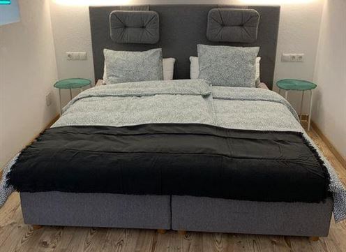 A modern bedroom with a large bed and two nightstands. The walls are light and the lighting is soft.