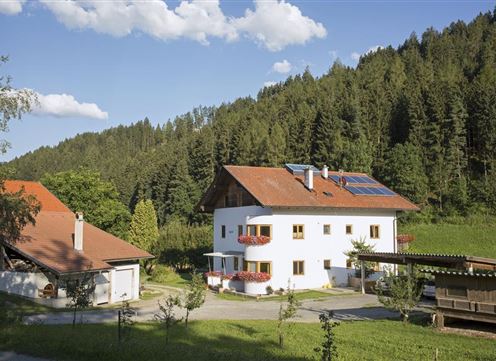 A modern house in a rural setting, surrounded by trees and meadows. The sky is clear with a few clouds.