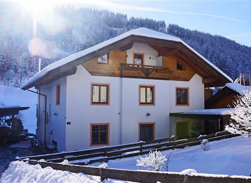 A charming house in the snow, surrounded by a wintry landscape. The sun shines brightly on the snow-covered roofs and the surrounding trees.