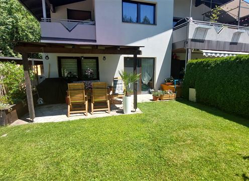 A well-maintained garden with green lawn and a terrace. In the background, there is a cozy house.