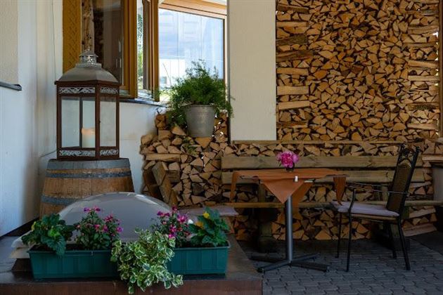 Un espace extérieur chaleureux avec une table et des chaises. À l'arrière-plan, on peut voir une pile de bois et des jardinières.