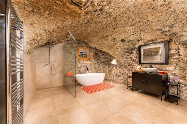 Ein modernes Badezimmer mit einer freistehenden Badewanne und einer Glasdusche. Die Wände bestehen aus natürlichem Gestein, was einen rustikalen Charme verleiht.