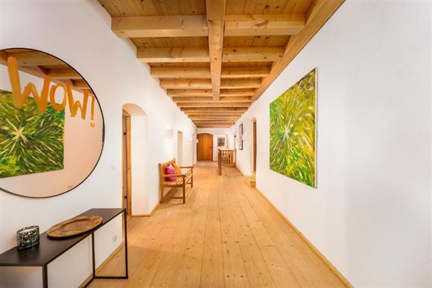 Ein heller Flur mit Holzboden und Holzdecke. An den Wänden hängen bunte Kunstwerke und ein runder Spiegel mit der Aufschrift „WOW!“.