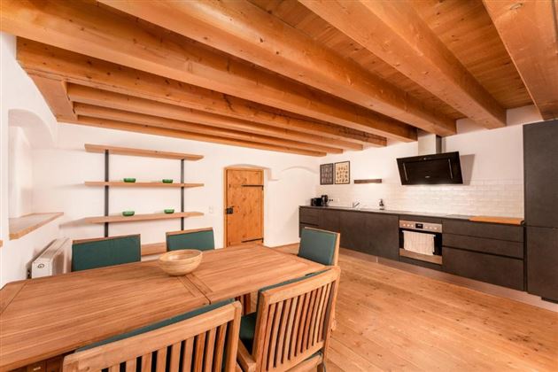 Eine moderne Küche mit Holzregalen und einem großen Esstisch. Die Wände sind hell, und die Holzdecke verleiht dem Raum eine gemütliche Atmosphäre.