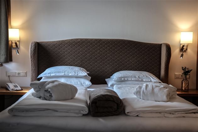 Ein gemütliches Hotelzimmer mit einem Doppelbett und zwei Kissen. Handtücher sind ordentlich aufgelegt, und sanfte Beleuchtung sorgt für eine entspannte Atmosphäre.