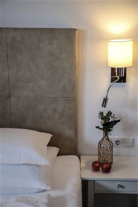 Ein gemütliches Schlafzimmer mit einem großen Kopfteil und einer modernen Leseleuchte. Auf dem Nachttisch stehen eine Vase mit Blumen und zwei Äpfel.