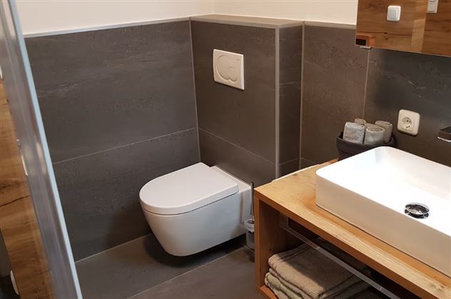 A modern bathroom with a toilet and a sink on a wooden table. The walls are in a dark gray tone.