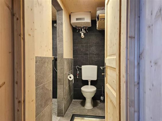 Ein modernes Badezimmer mit einem Toilettenraum und eleganten Fliesen. Die Wände sind teilweise aus Holz und die Beleuchtung sorgt für eine einladende Atmosphäre.
