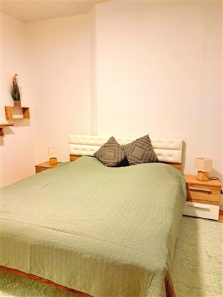 A bedroom with a large bed and two nightstands. The walls are plain and the bedding is green.