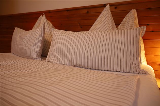 Ein gemütliches Schlafzimmer mit gestreiften Kissen auf einem Bett. Die warmen Holzwände verleihen dem Raum eine einladende Atmosphäre.