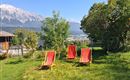 Een zonnige tuin met drie rode ligstoelen en uitzicht op de bergen. De natuur is groen en uitnodigend.