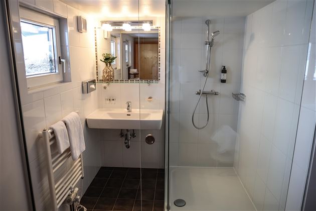 Ein modernes Badezimmer mit einer Dusche und einem Waschbecken. Die Wände sind hell gefliest, und es gibt einige Pflanzen zur Dekoration.