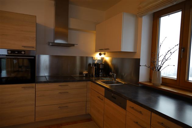 Eine moderne Küche mit Holz- und Metalloberflächen. Das Fenster bietet Sicht nach draußen und lässt Tageslicht herein.