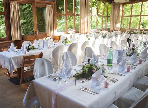 Une table élégamment décorée avec des nappes blanches et des arrangements floraux. La pièce a de grandes fenêtres qui laissent entrer beaucoup de lumière naturelle.