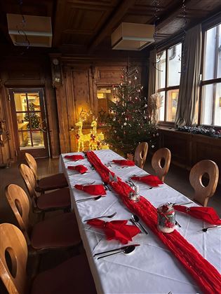 A festively set table in a cozy room. In the background, there is a Christmas tree with lights and decorations.