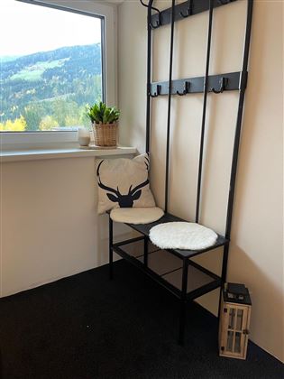 Un hall d'entrée confortable avec un banc et un coussin décoratif. En arrière-plan, il y a des fenêtres et un joli paysage.