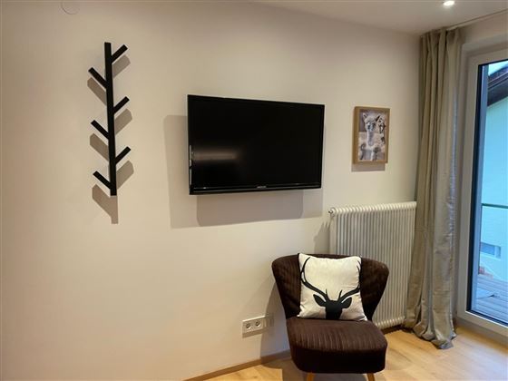 Un espace de vie confortable avec une télévision au mur. Un rocking-chair et un vestiaire moderne complètent la décoration.