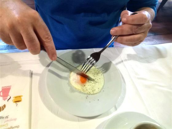 A plate with scrambled eggs and a yellow yolk. A hand is holding cutlery to portion the food.