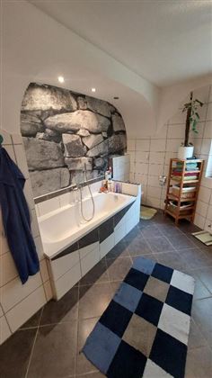 Ein modernes Badezimmer mit einer Badewanne und einem Steinmuster an der Wand. Auf dem Boden liegt ein stilmatten in Blau und Weiß.