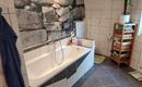 Ein modernes Badezimmer mit einer Badewanne und einem Steinmuster an der Wand. Auf dem Boden liegt ein stilmatten in Blau und Weiß.